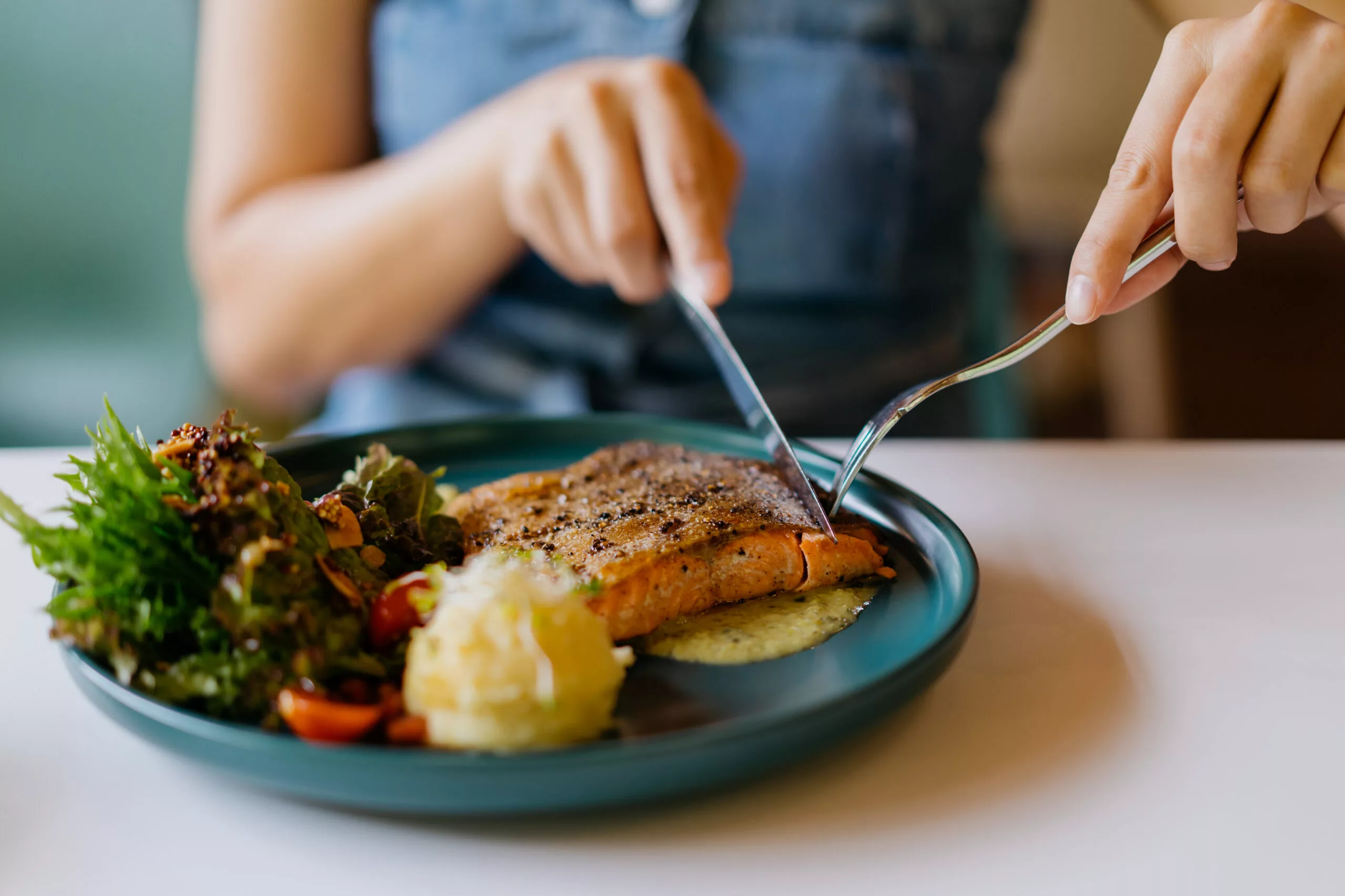 Close up shot of an Asian Chinese woman eating pan fried salmon with table knife and fork in cafe