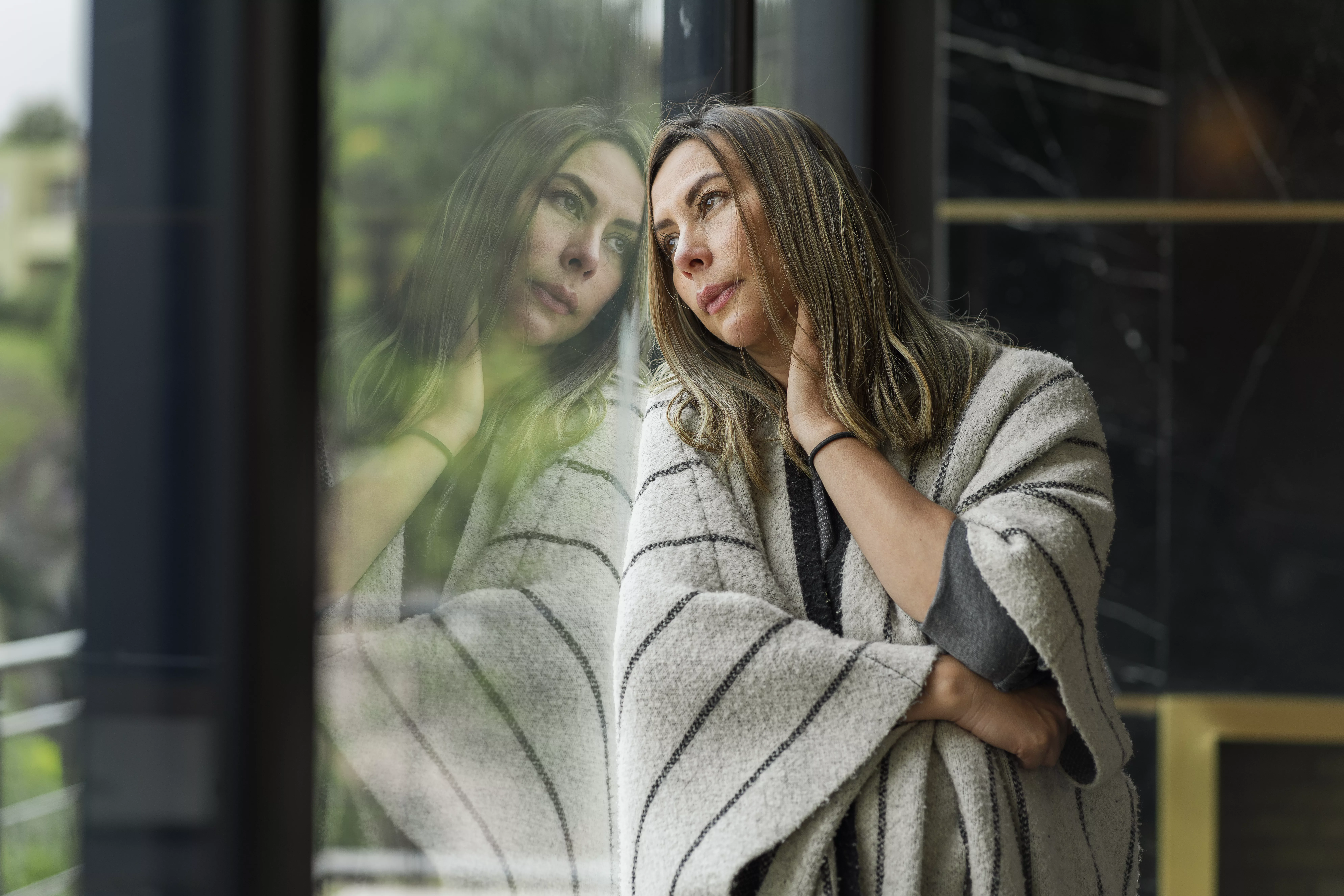 Latin woman from Bogota Colombia between 30 and 34 years old, very bored and sad leaning on the window of her house looking away from so much time of isolation