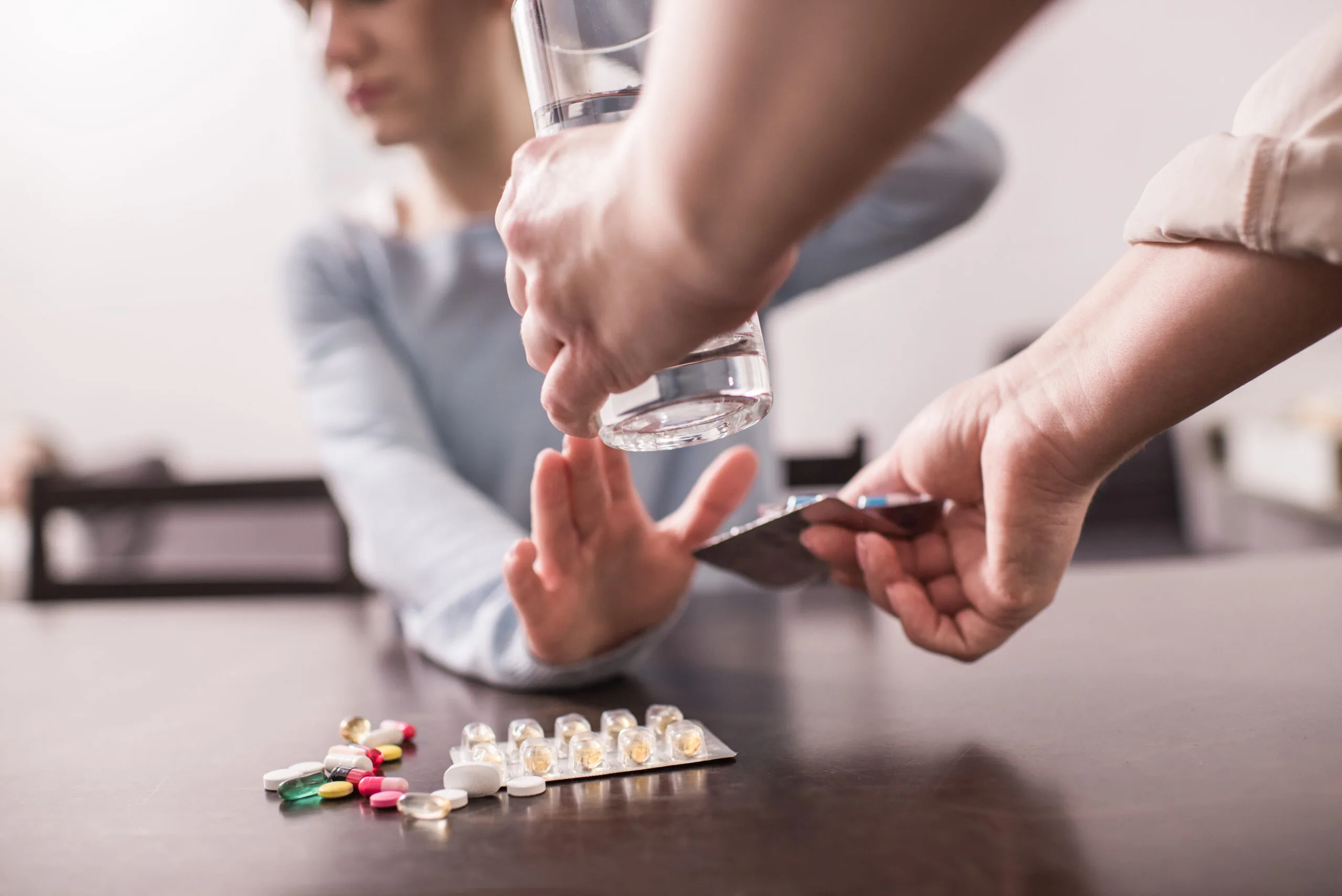 cropped shot of mother bringing glass of water and medicine to sick adult daughter