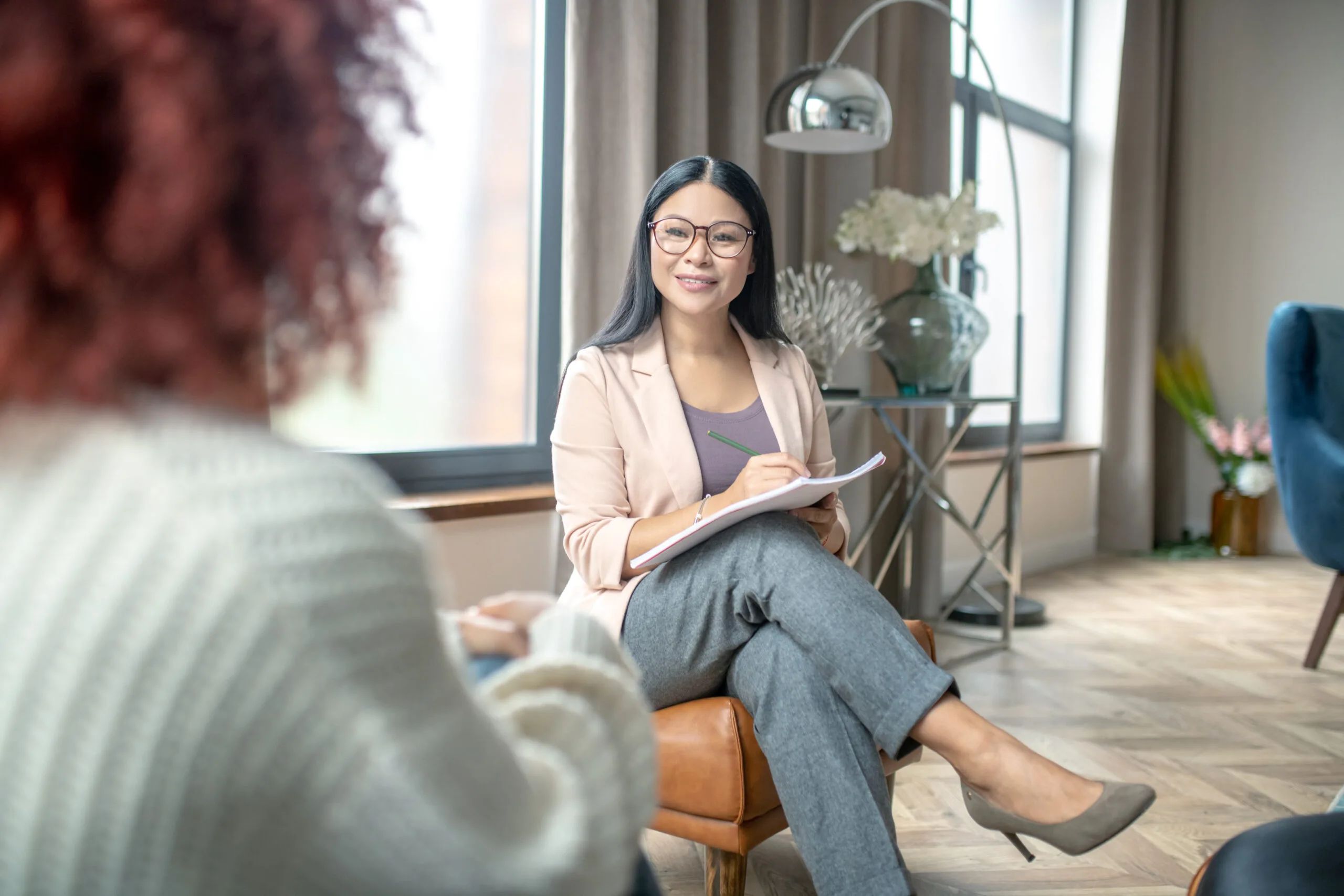 Pleasant psychologist. Pleasant psychologist wearing grey trousers smiling to client while speaking with her